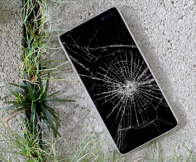 Cracked Samsung phone screen on concrete near grass. Repair needed. ER4Gadgets