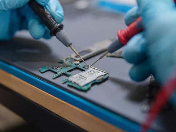 Electronics repair: Close-up of gloved hands repairing a circuit board with precision tools. ER4Gadgets